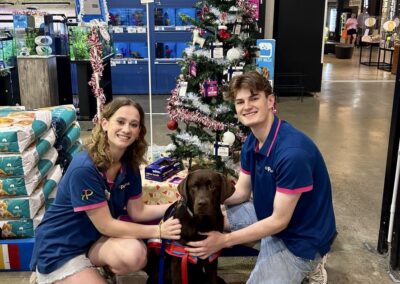 Two Petstock employees kneel next to Assistance Dog inside store