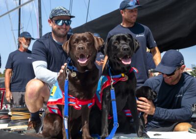 Brown and black labrador Ambassador Assistance Dogs sit in front of two crew members on board the Celestial V70 yacht