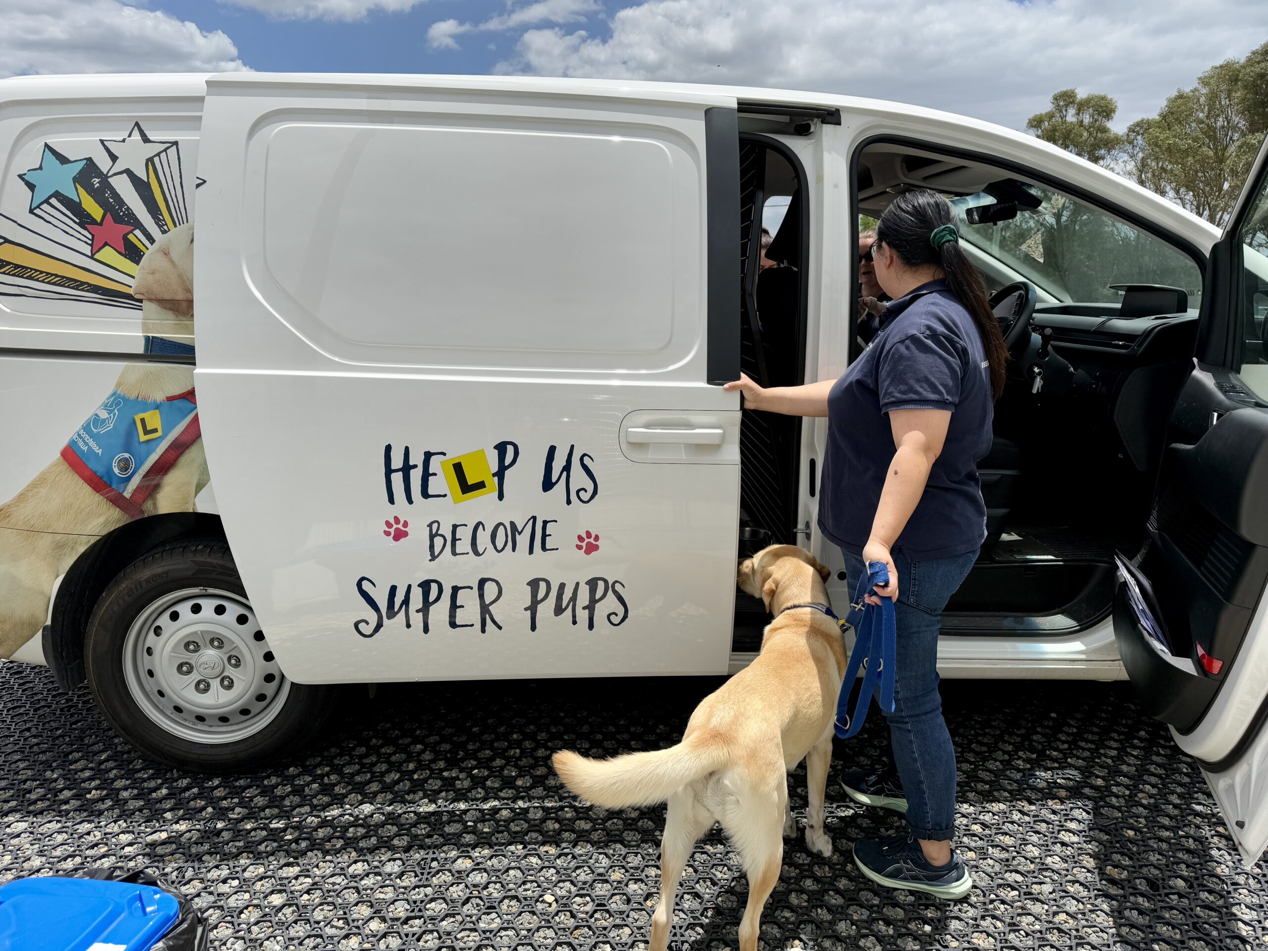 Dog trainer with labrador assistance dog standing next to her opening door of Hyundai van for dog to jump in