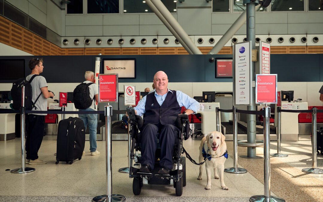 Man in wheelchair facing camera with his assistance dog at the airport