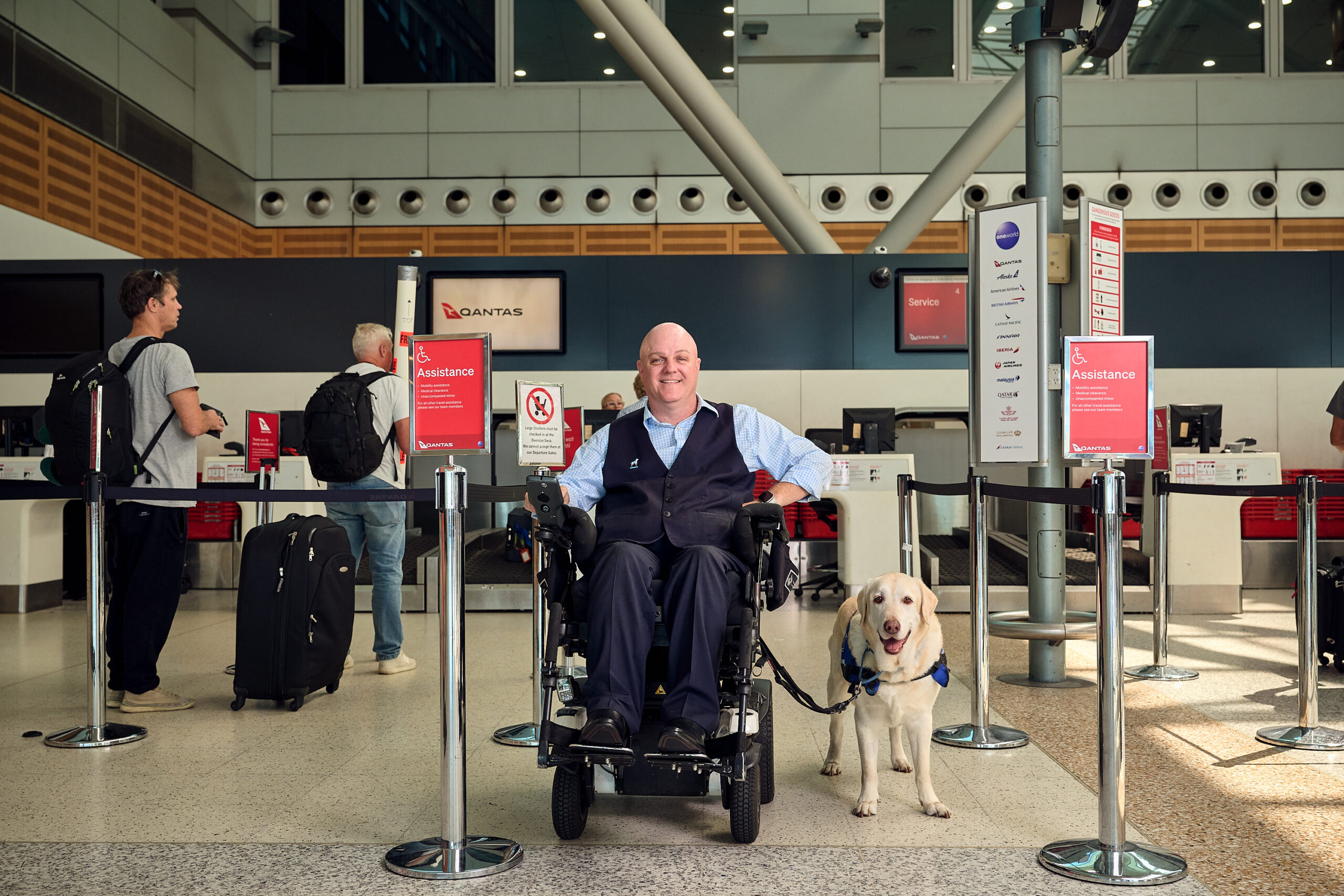 Man in wheelchair facing camera with his assistance dog at the airport